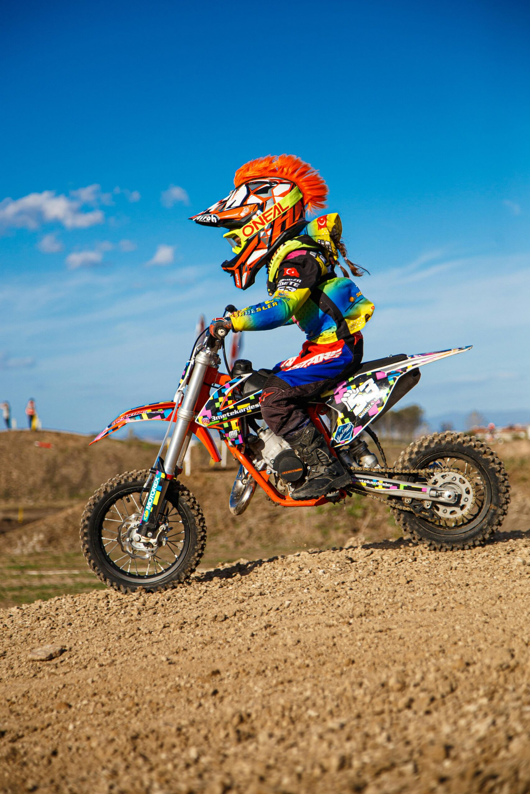 Young racer on a dirt bike with helmet and gear, speeding on a gravel track.